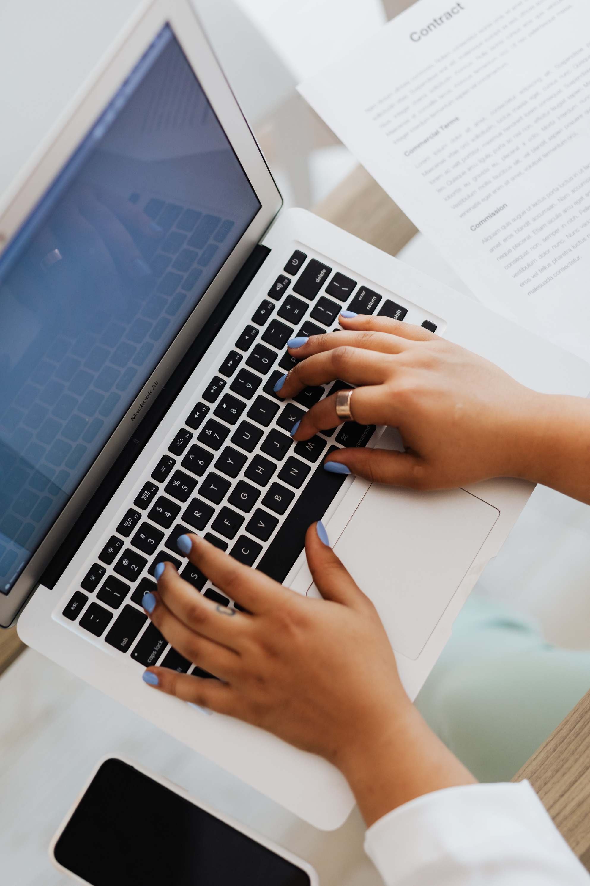 Hands reviewing figures on a laptop, typing at a workspace with documents